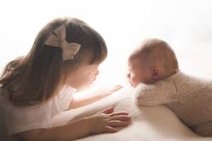 big sister looking deep into newborn baby brothers eye.